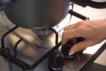 Hand woman opening gas burning from a kitchen gas stove.