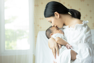 Young Asian mother holding newborn baby and kissing, maternity concept, soft image of beautiful family