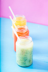 freshly squeezed fruit juice, smoothies yellow orange green on bright blue and pink background Close up