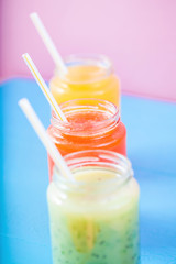 freshly squeezed fruit juice, smoothies yellow orange green on bright blue and pink background Close - up