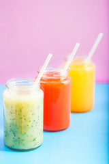 freshly squeezed fruit juice, smoothies yellow orange green on bright blue and pink background Close - up