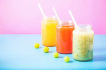 freshly squeezed fruit juice, smoothies yellow orange green grape on bright blue and pink background Copy space