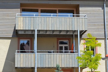 Moderne, neu gebaute Balkone in aufgeständerter Stahlrahmenkonstruktion und mit lasiertem Holz beplankt an der Fassade eines renovierten Altbau-Wohnhauses