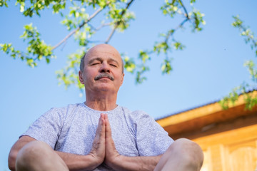 Peaceful senior man meditating seated ooutdoor under the tree. Concept of mental health