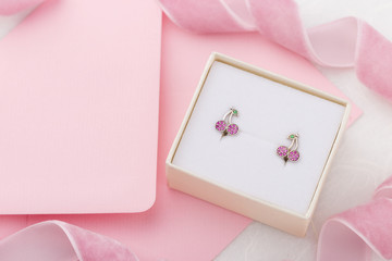 Cherry shaped earrings with crystals in gift box on pink envelope background with copy space