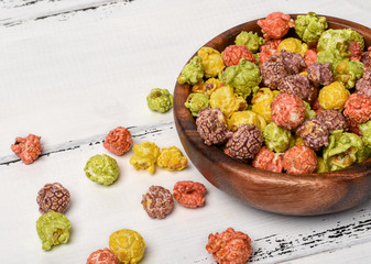 Colorful caramel popcorn in a wooden bowl on a white wooden background