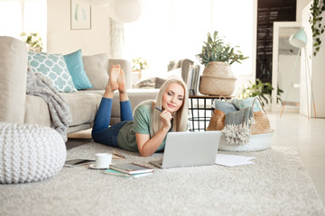 Pleased young woman using a laptop in living room