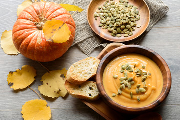 Pumpkin soup in a wooden bowl, with autumn leaves and pumpkin