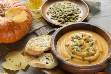 Pumpkin soup in a wooden bowl, with autumn leaves and pumpkin