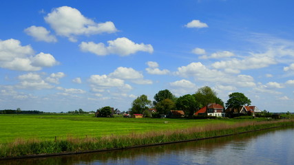 Fototapeta na wymiar flache Landschaft in Friesland mit Kanal, grünen Wiesen, Bauernhöfen und herrlichen Wolken