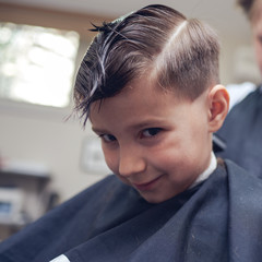 Caucasian boy getting hairstyle by hairdresser in barbershop.