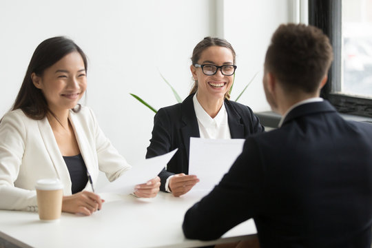 Positive multiracial hr team or friendly female executives laughing at funny joke during successful job interview with male winning applicant making good first impression, humor and hiring concept