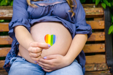 Pregnant woman shows on camera heart LGBT Pride Rights Lesbian Gay Bisexual Transgender Geek on city sunny day background. Pride mounth day