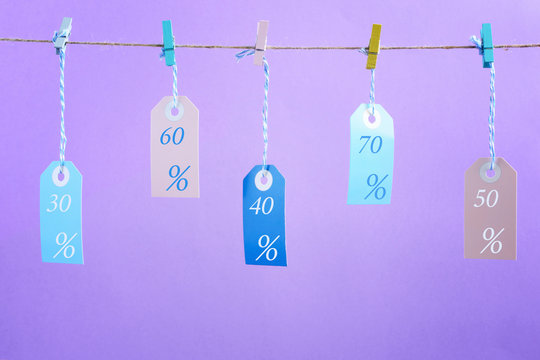 On lilac background photographed labels. Five multicolored empty labels hang on a rope pinned with clothespins. Each label has a discount of twenty-five, thirty, fifty percent. Bright layout mock up. - Powered by Adobe