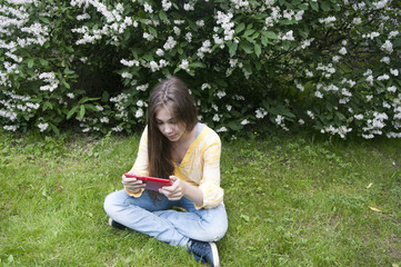Beautiful teenager girl with tablet computer sits on the grass in Park. Photo