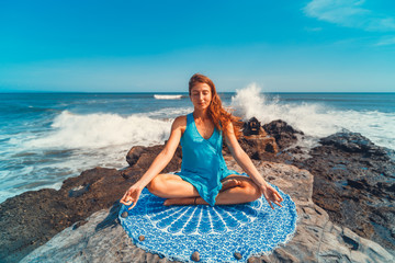 Young caucasian woman doing yoga exercises on the cliff by the ocean at dawn