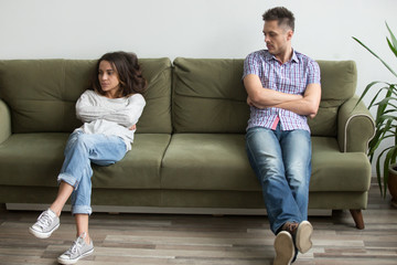 Frustrated millennial couple sit apart on couch in living room not talking after fight, unhappy boyfriend and girlfriend having disagreement thinking of bad relationships, marriage problems concept