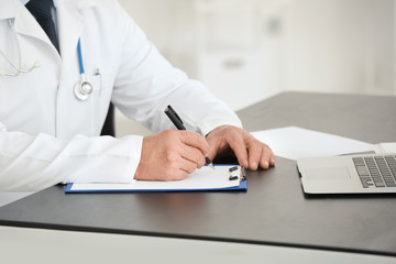 Fototapeta premium Male doctor filling up application form in consultation room, closeup
