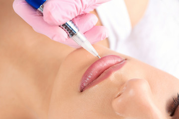 Obraz na płótnie Canvas Young woman getting permanent makeup on lips in beautician salon, closeup