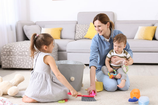 Housewife with little children cleaning carpet in room