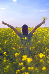 a happy girl in a cap and in round glasses runs around the field with yellow flowers and laughs, jumps and has fun. A girl is smiling on a flowering field.