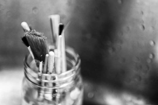 Black and white image of paint brushes in a glass mason jar.