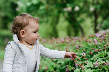 White blonde female toddler touching small pink flower.