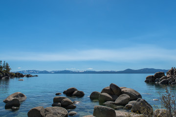 Rocks in Lake Tahoe with snow capped mountains in background.
