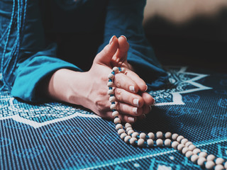Concentrated woman praying with wooden rosary beads on yoga mat with mandala. Namaste. Close up...