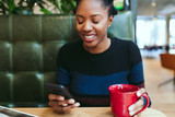 Young businesswoman using smartphone while having coffee in the office