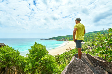 an adventure man hiking on neautifully shaped granite boulders and watching grand anse beach, la digue island, seychelles - obrazy, fototapety, plakaty