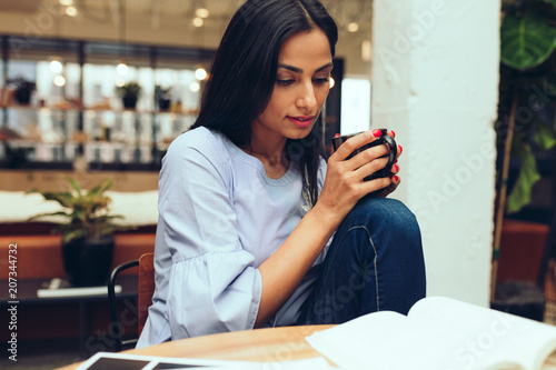 Young businesswoman reading a book while having coffee