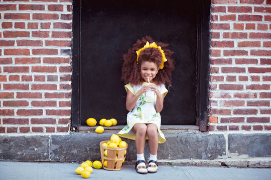 Portrait of happy girl sitting on doorstep with basket of lemons