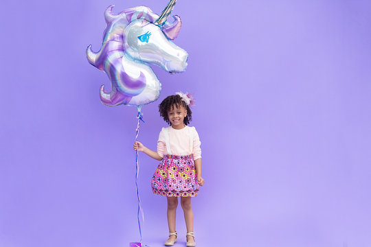 Girl holding unicorn balloon against purple background