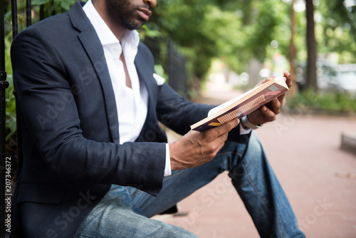 Low section of businessman reading book while sitting outdoors