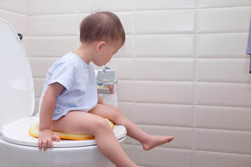 Cute little Asian 2 year old toddler baby boy child sitting on the toilet modern style with a kid...