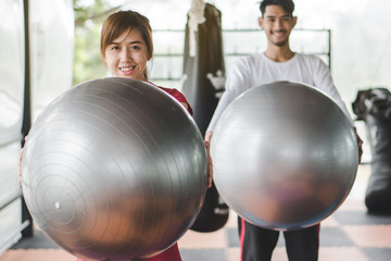 Healthy Body ball training workout. Young cheerful asian woman  holding ball and enjoying exercise in gym with friend.
