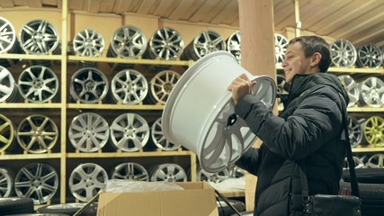Obraz na płótnie Canvas The man buys alloy wheels in his shop for his car. He takes a disc out of the box and looks at it. The white wheel is very beautiful and steep. Drawing and form of the disc are thin knitting needles