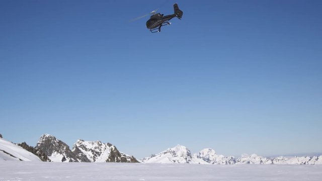 Black helicopter taking off from snowy mountains in slow motion