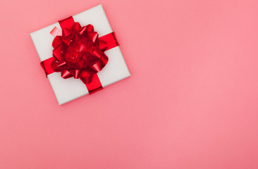 White gift box with red satin bow and ribbon on pastel pink background with copy space