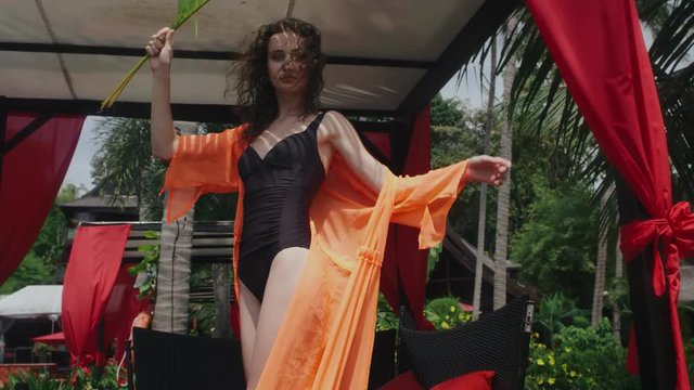 Model posing in an orange pareo under palm trees