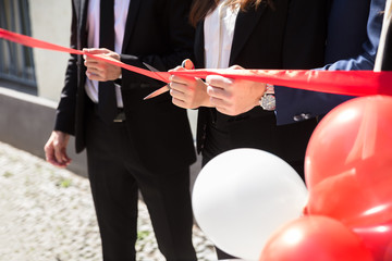 Businesspeople Hand Cutting Red Ribbon