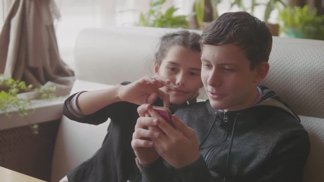 children are sitting in a cafe playing games in the smartphone slow motion video. boy and girl teens social media on smartphone. kids children and smartphone lifestyle concept