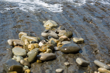 pebble stones on the sea beach, the rolling waves of the sea with foam