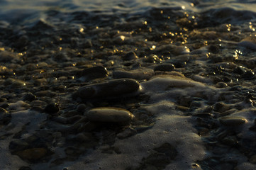 pebble stones on the sea beach, the rolling waves of the sea with foam