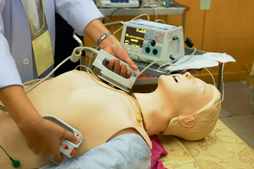 A female physician performning cardioversion with defibrillator on a mannequin during advance cardiac life support course training - obrazy, fototapety, plakaty