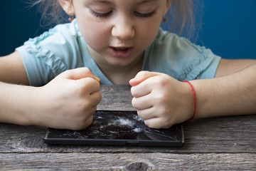 evil little girl blows her fists on a smartphone, breaks it