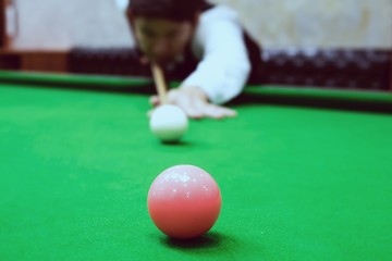 Asian man playing snooker aiming his cue stick at a white cue ball - snooker player in competition match concept