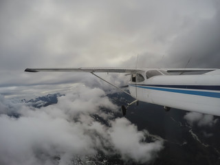 Fototapeta premium Airplane flying over the beautiful Canadian Mountain Landscape during a cloudy evening. Taken North of Vancouver, British Columbia, Canada.
