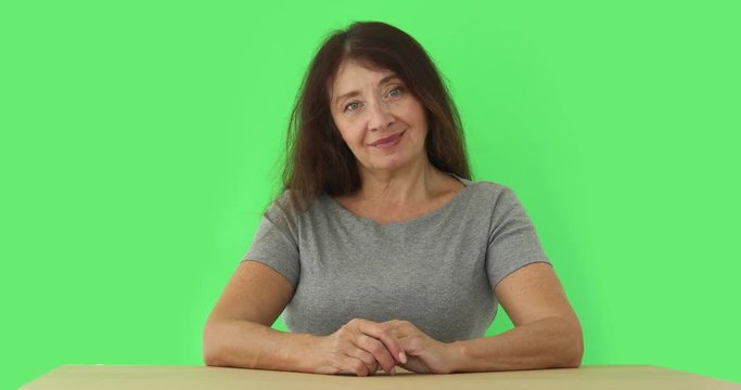 Beautiful mid aged caucasian woman sitting and smiling at table on green background